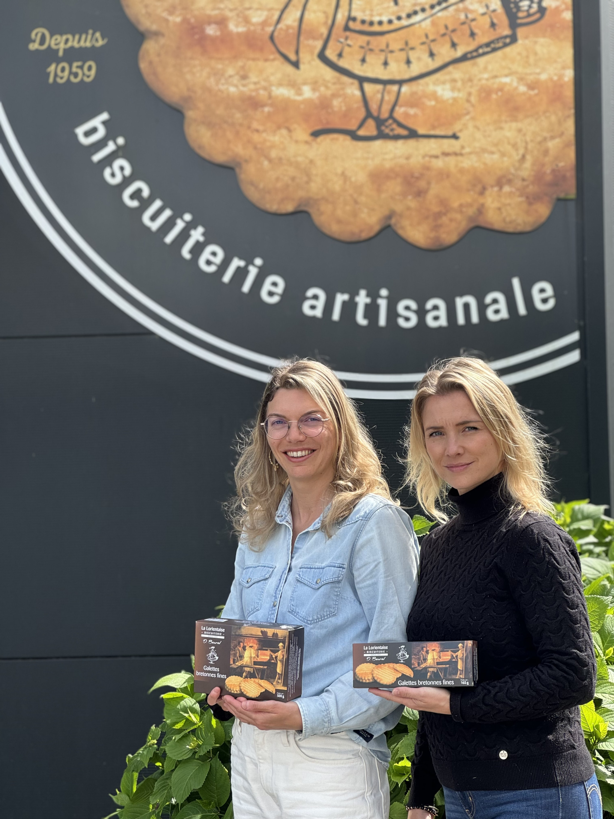Les deux sœurs Beurel posent devant leur biscuiterie et présentent des paquets de gâteaux (Kervignac, Morbihan, 56)