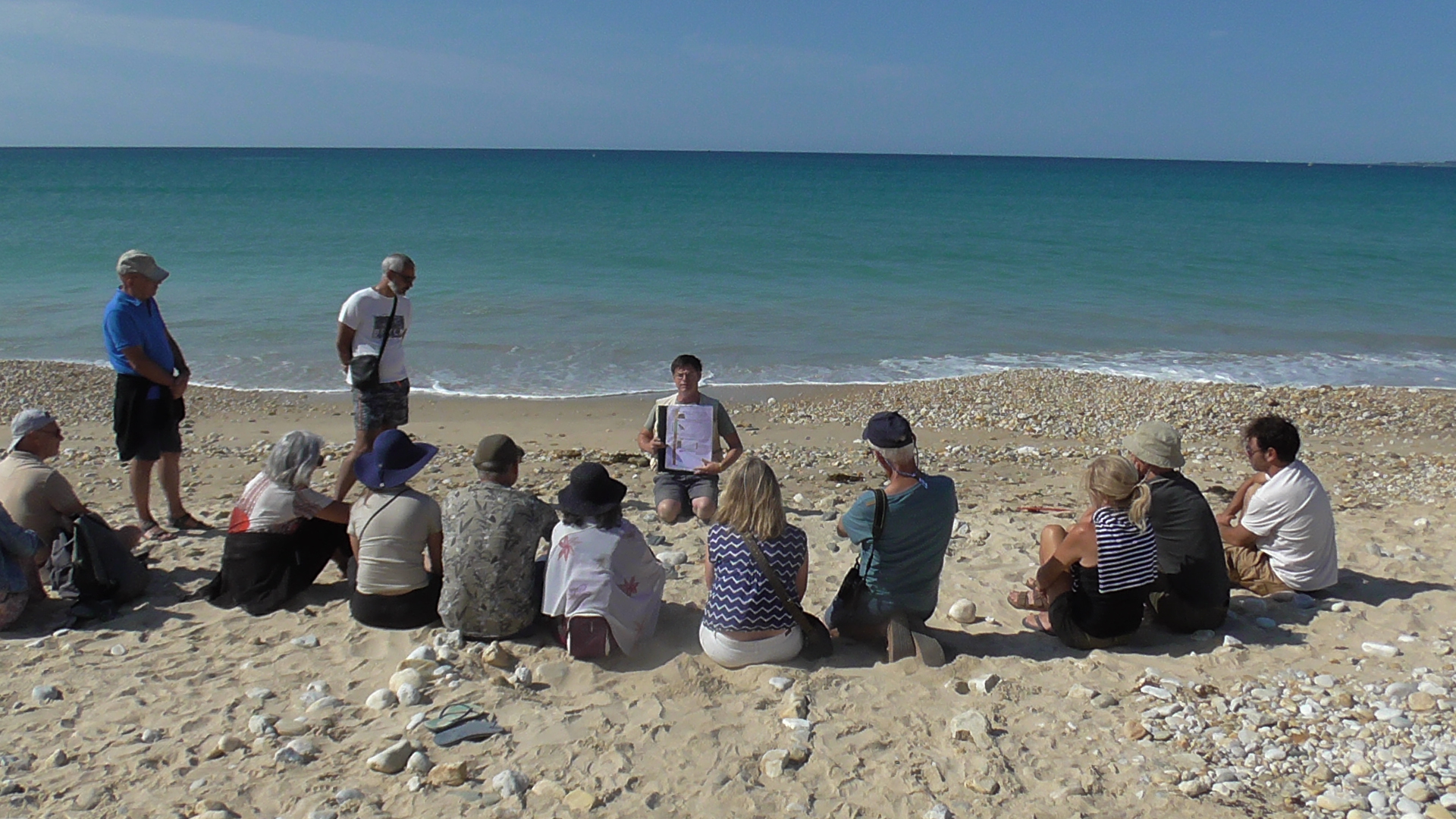 Samuel Piriou, géologue et animateur scientifique, présente un atelier devant un groupe d’une douzaine de personnes, sur une plage (Plouhinec, Morbihan, 56)