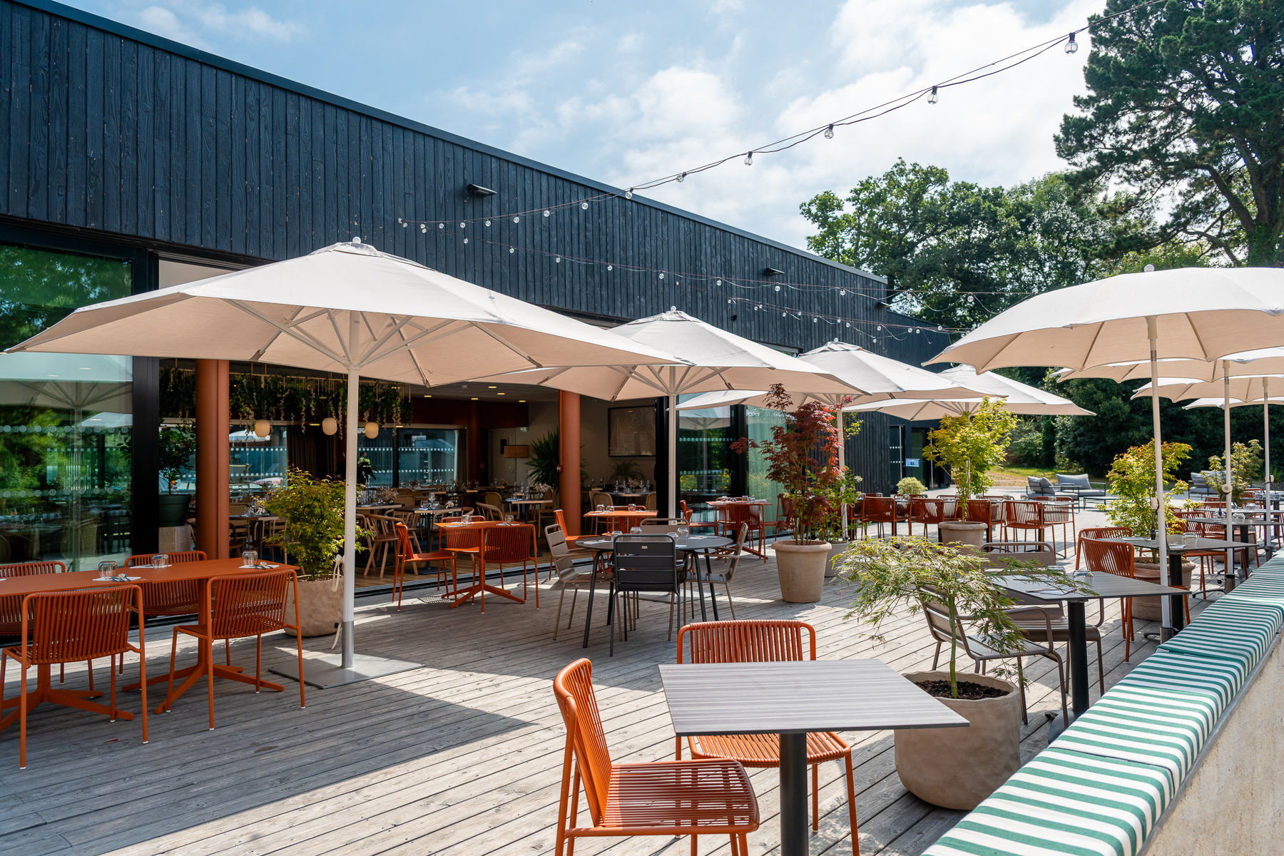 Vue extérieure sur la terrasse du restaurant, parquet en lame, tables, chaises et parasols (Le Bono, Morbihan, 56)