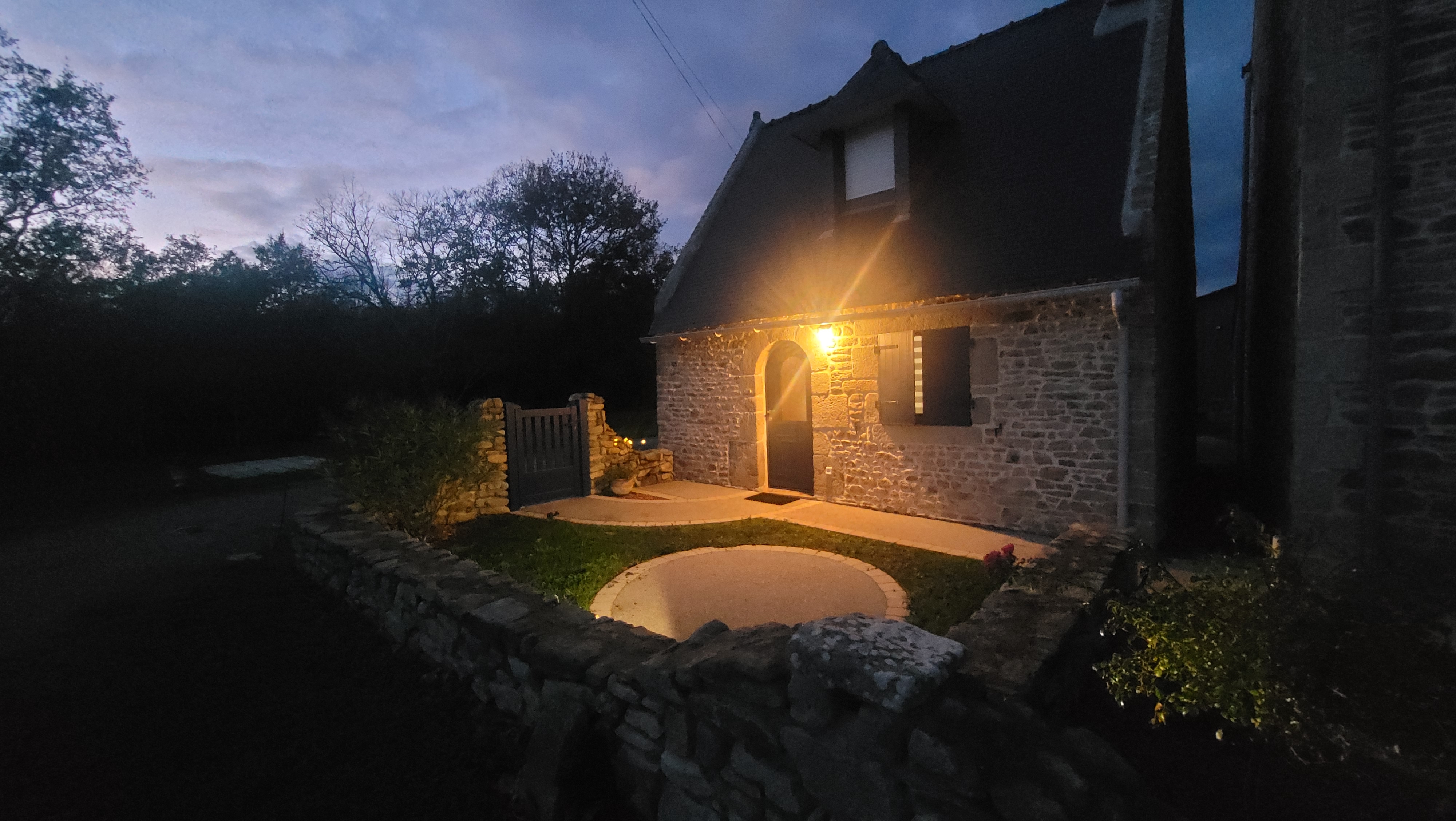 Façade du gîte vue à la tombée de la nuit, petite maison en pierre et sa cour privée (Merlevenez, Morbihan, 56)