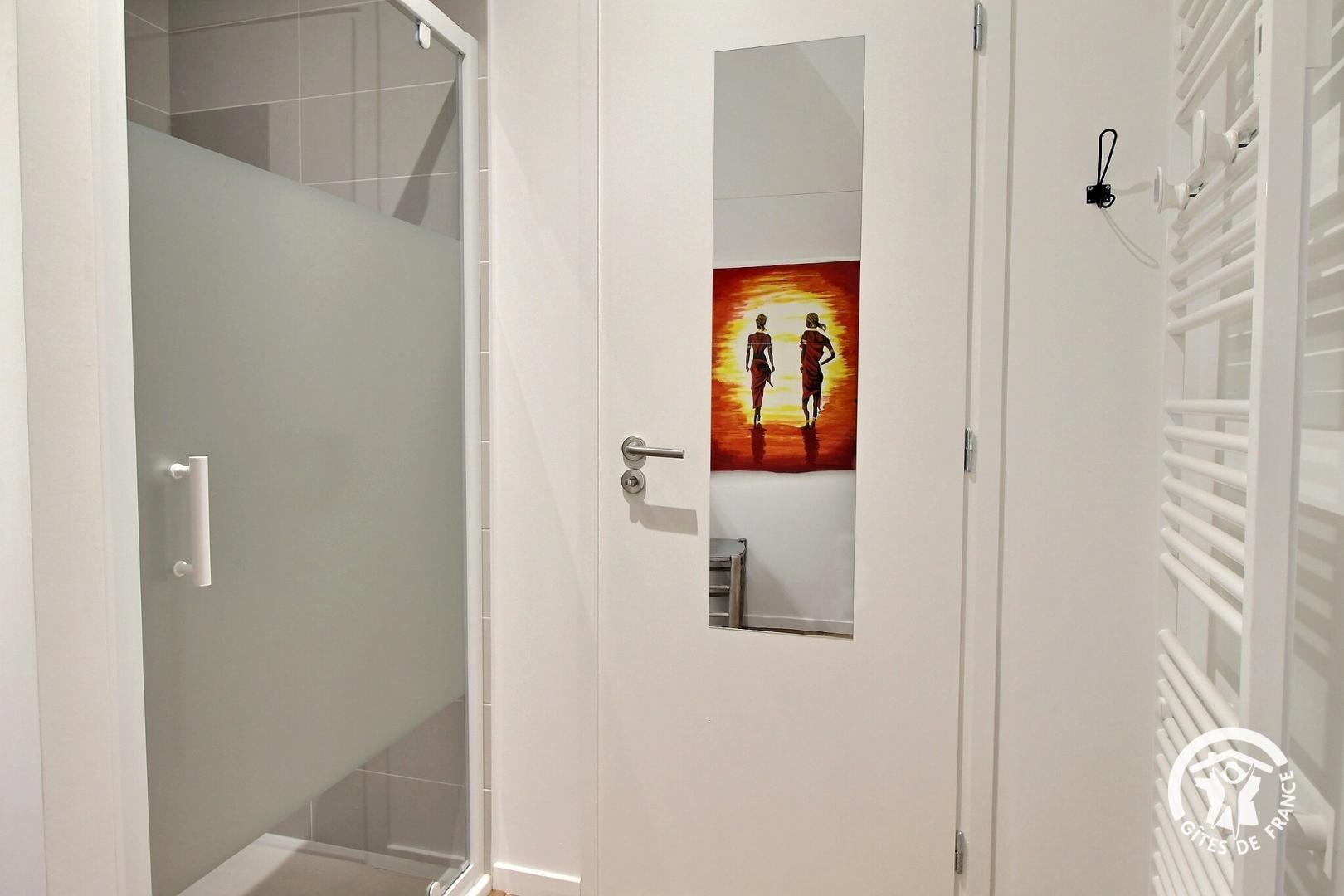 Gros plan dans la salle de bain et plus particulièrement sur la cabine de douche et le sèche-serviettes blanc, reflet du tableau africain coloré (Sainte-Hélène, Morbihan, 56)