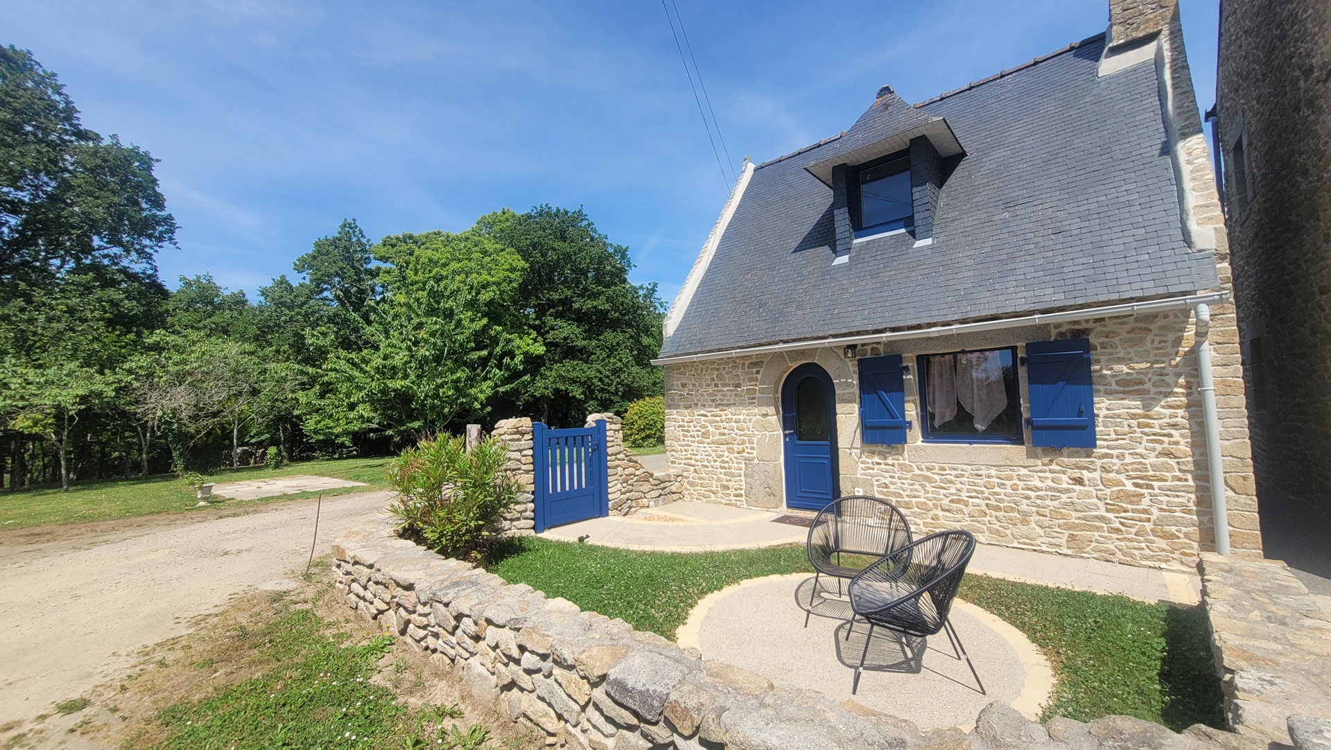 Principale –Façade en pierre et volets bleu bretagne du gîte, petite cour privée et salon de jardin (Merlevenez, Morbihan, 56)