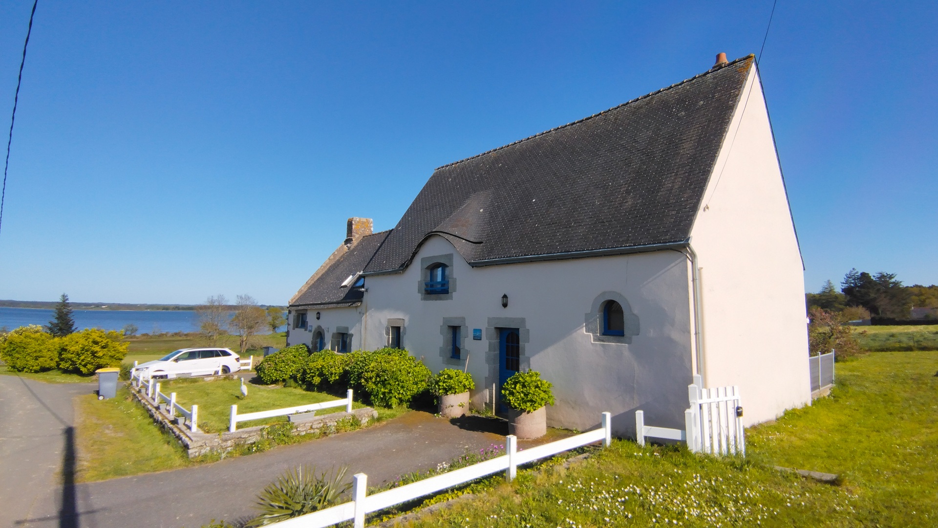 Principale - Façade extérieure du gîte La Grande Aigrette, maison néo-bretonne, allée goudronnée, jardinet et vue sur la ria d’Etel (Sainte-Hélène, Morbihan, 56)
