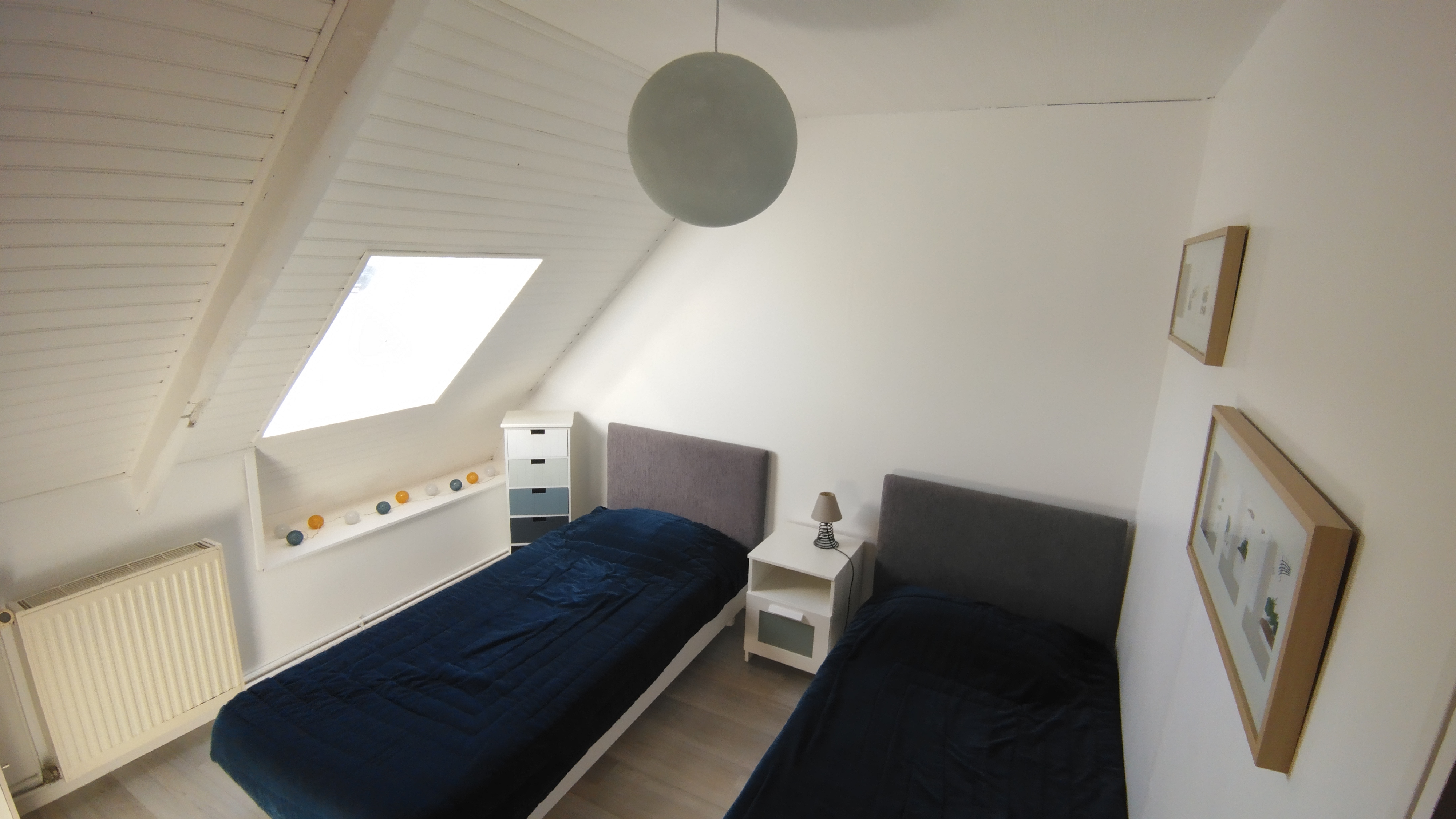 Une chambre sous plafond mansardé aux tons clairs avec deux lits simples, décoration minimaliste (Sainte-Hélène, Morbihan, 56)