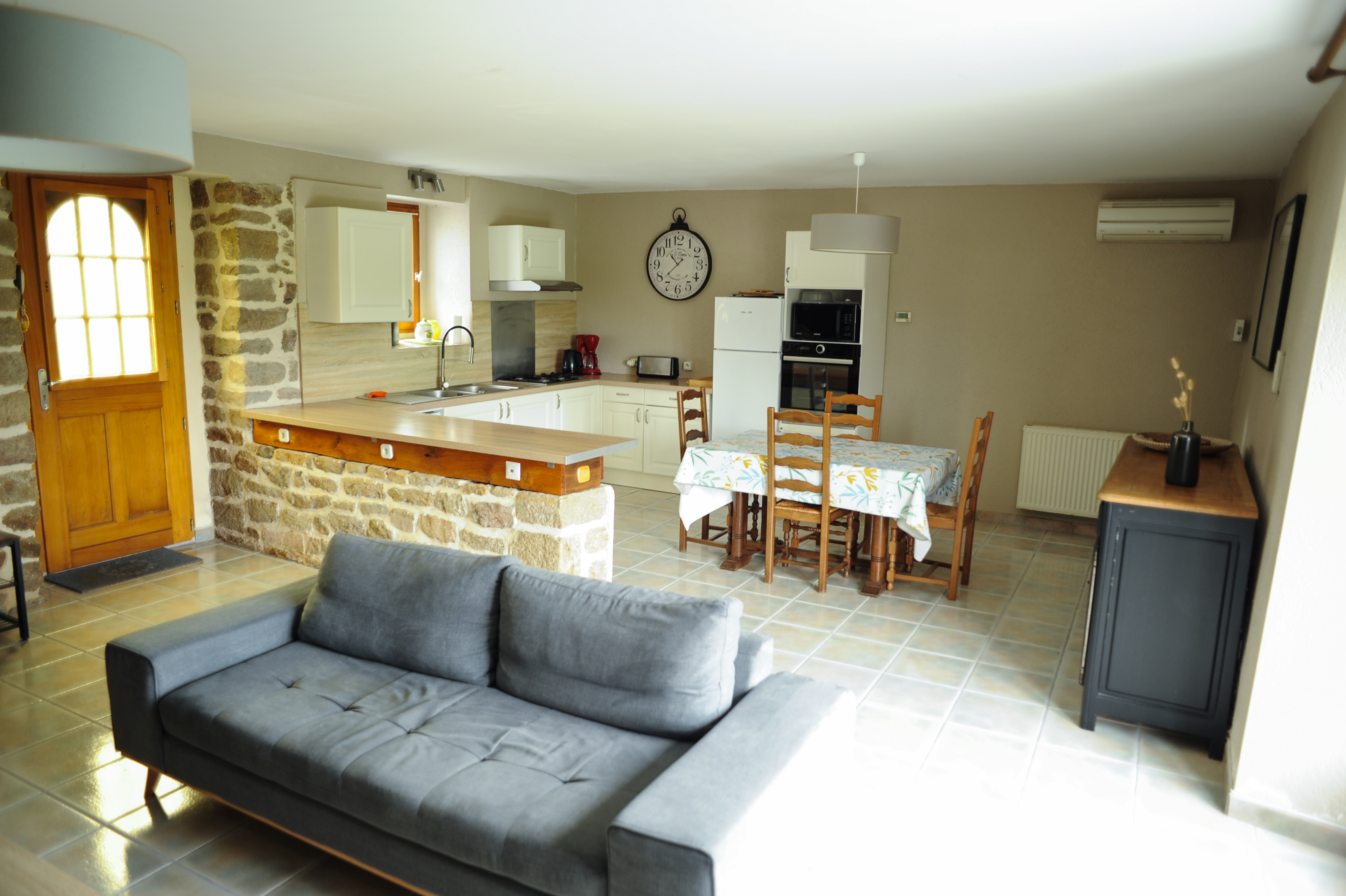 Vue sur le salon, la cuisine équipée et la salle-à-manger, mur en pierres apparentes, décoration minimaliste (Sainte-Hélène, Morbihan, 56)